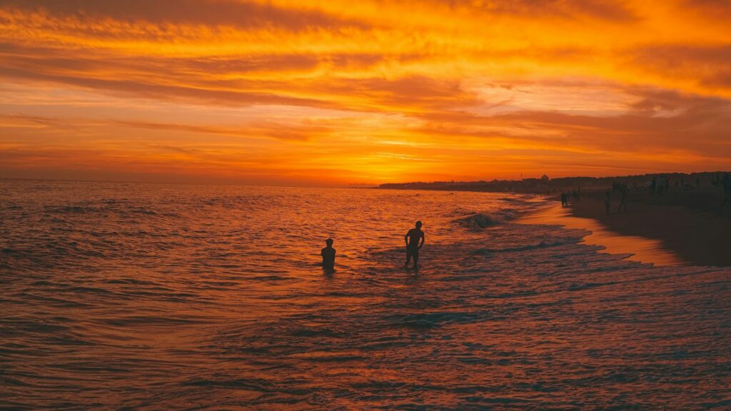 a couple of people standing on top of a beach next to the ocean